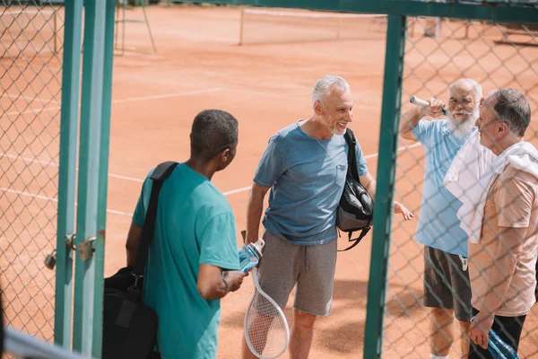 Gruppo multietnico di amici anziani con attrezzature da tennis in campo — Foto stock