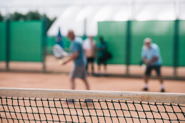 Selective focus of net and tennis players playing tennis on court — Stock Photo