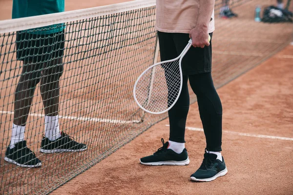 Cropped shot of interracial friends with tennis racquet standing near net — Stock Photo