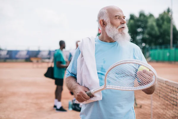 Selective focus of bearded old man with towel and tennis racquet on court — Stock Photo