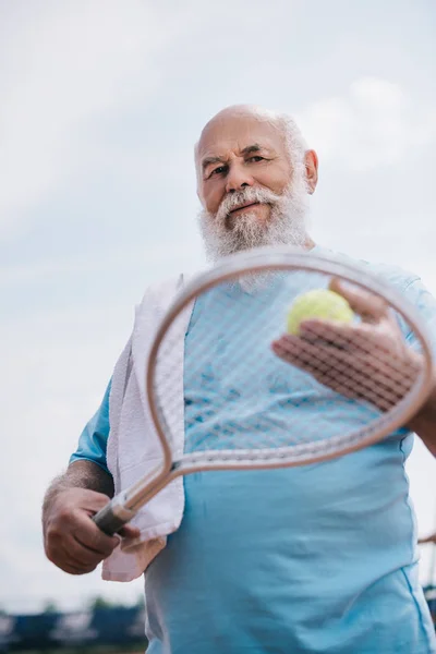 Vista de ángulo bajo del hombre viejo con toalla y equipo de tenis en las manos - foto de stock