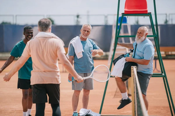 Selective focus of old multiethnic friends on tennis court on summer day — Stock Photo