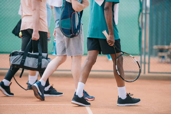Частковий вид на багатокультурних літніх чоловіків з тенісним обладнанням, що ходить на корті — стокове фото