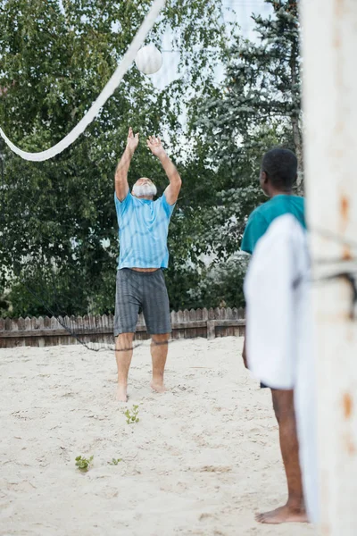 Selective focus of multiethnic old men playing volleyball together on beach — Stock Photo