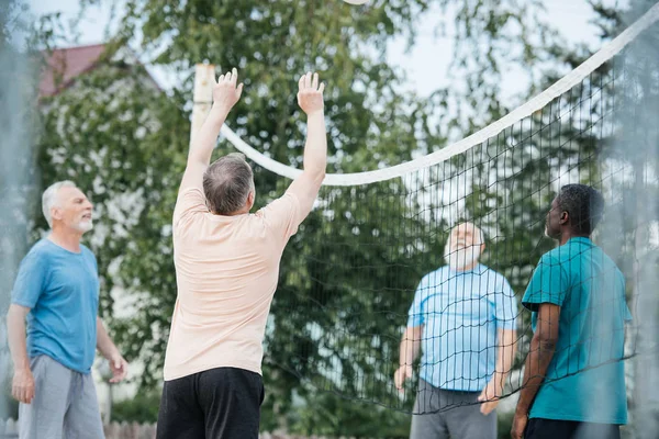 Multikulturelle alte Freunde spielen an einem Sommertag am Strand Volleyball — Stockfoto