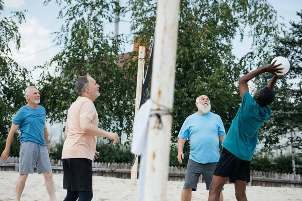 Side view of multicultural old friends playing volleyball on beach on summer day — Stock Photo