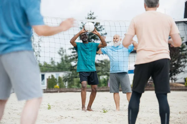 Partial view of multicultural old friends playing volleyball on beach on summer day — Stock Photo