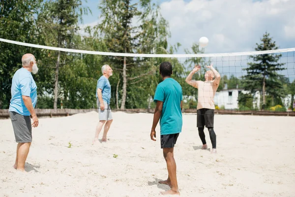 Multicultural old friends playing volleyball on beach on summer day — Stock Photo