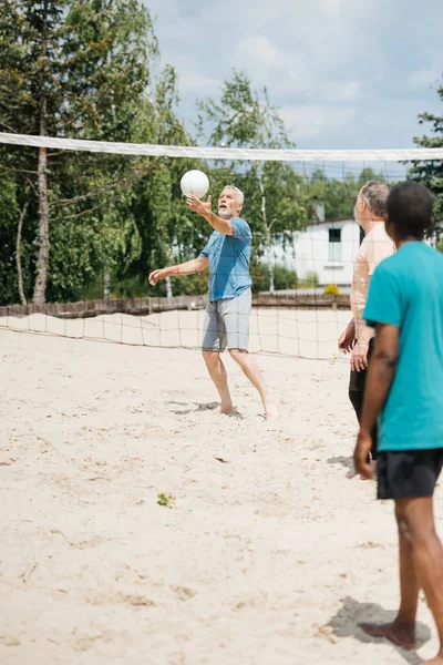 Selective focus of multiethnic old men playing volleyball together on beach — Stock Photo