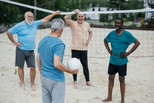 Многокультурные старые друзья играют в волейбол на пляже в летний день — стоковое фото