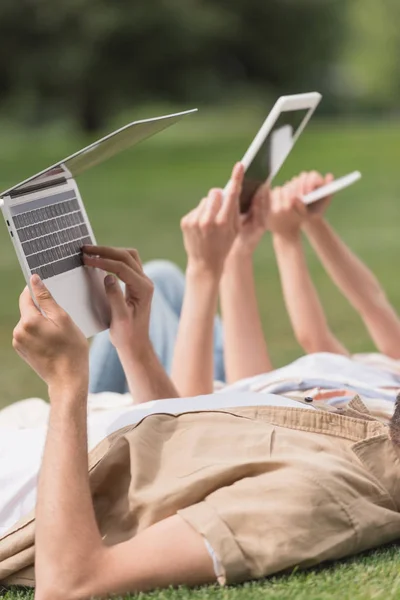 Plan recadré de la famille en utilisant des appareils numériques tout en étant allongé sur la pelouse dans le parc — Stock Photo