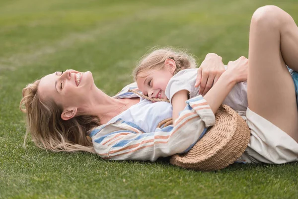 Glückliche Mutter und Tochter umarmen sich im grünen Gras im Park — Stockfoto