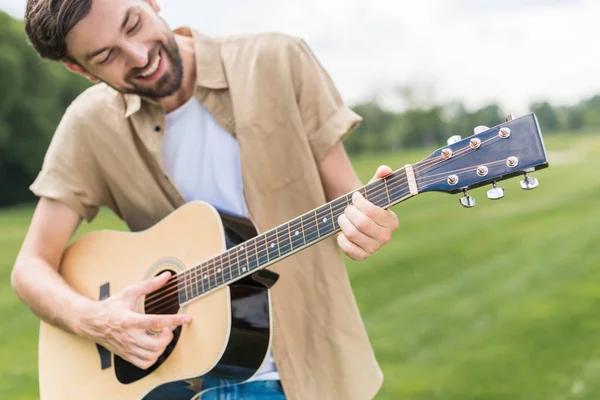 Felice giovane che suona la chitarra acustica nel parco — Foto stock