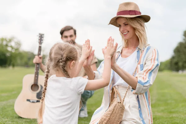 Счастливая мать и дочь играют вместе, пока отец держит акустическую гитару в парке — стоковое фото