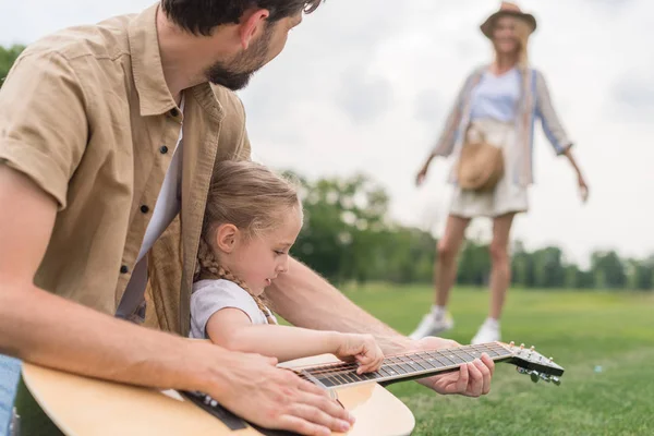 Recortado disparo de padre e hija tocando la guitarra mientras madre de pie detrás en el prado - foto de stock