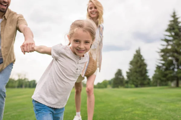 Cropped shot of parents with daughter holding hands and child smiling at camera in park — Stock Photo