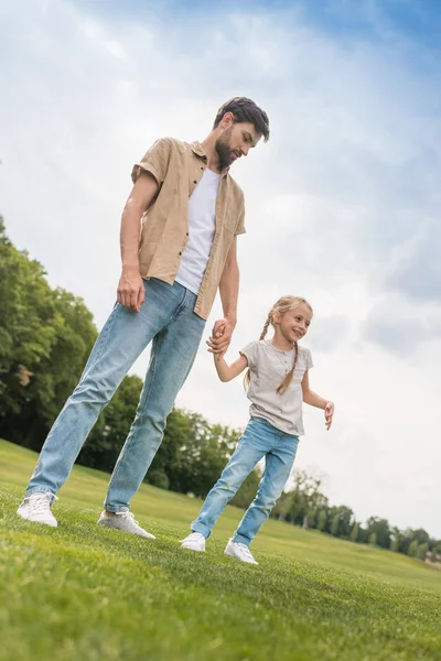 Vista de ángulo bajo del padre y la pequeña hija tomados de la mano mientras pasan tiempo juntos en el parque - foto de stock