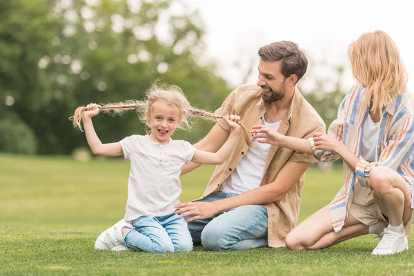 Padres felices mirando adorable pequeña hija divertirse y sonreír a la cámara en el parque — Stock Photo