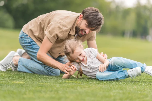 Щасливий батько і дочка розважаються разом на зеленому газоні в парку — стокове фото