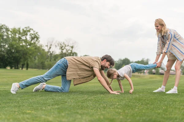 Vista lateral da família feliz se divertindo na grama verde no parque — Fotografia de Stock