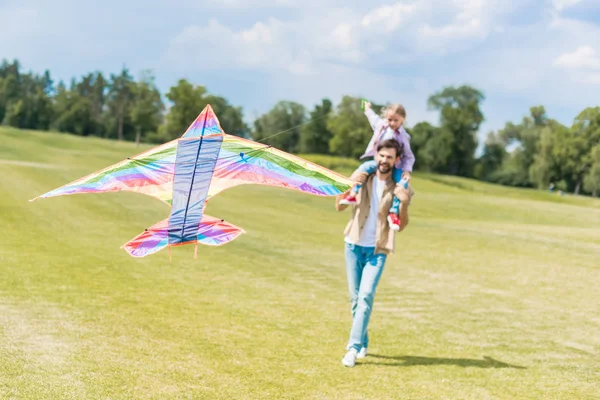 Feliz padre y linda hijita jugando con colorido cometa en el parque - foto de stock