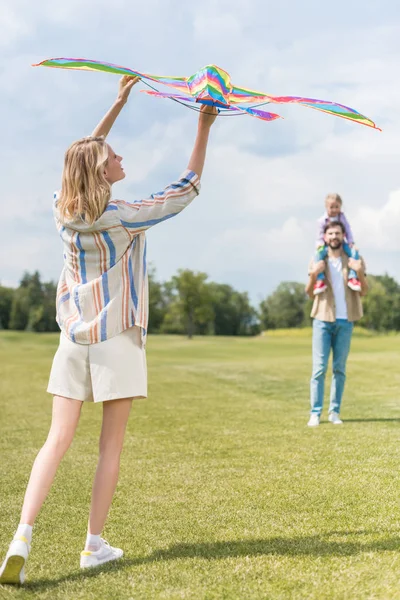 Junge Frau hält bunten Drachen, während Vater kleine Tochter am Hals trägt — Stockfoto