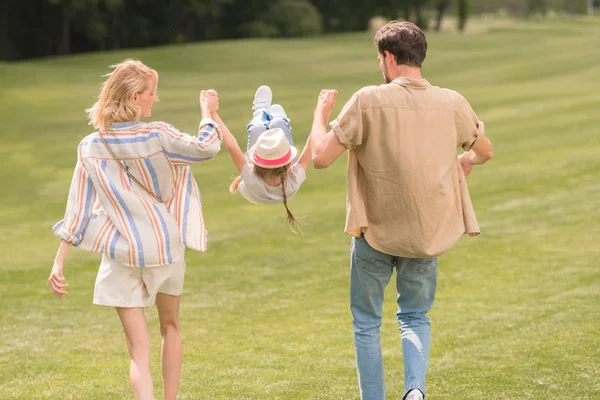 Rückansicht von Eltern mit kleiner Tochter, die Händchen halten und Spaß beim gemeinsamen Spaziergang im Park haben — Stockfoto