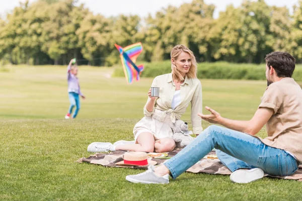 Parents sitting in plaid at picnic while daughter lying behind in park — Stock Photo