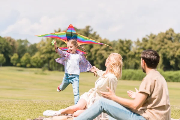 Família feliz com uma criança brincando com pipa colorida no parque — Fotografia de Stock