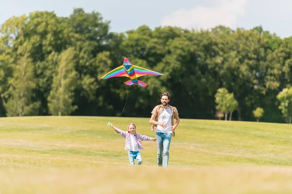 Glücklicher Vater und Tochter laufen auf Wiese und spielen mit Drachen — Stockfoto