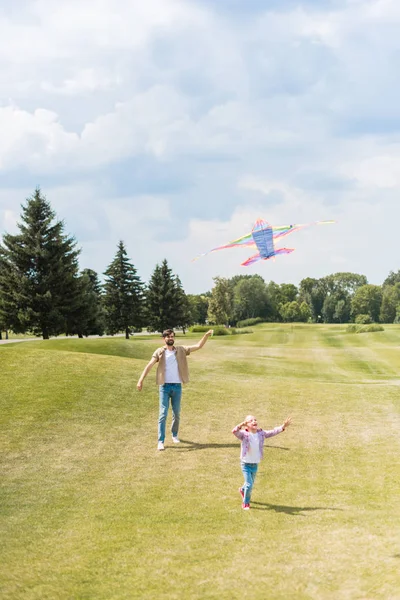 Happy father and daughter playing with kite and running on lawn in park — Stock Photo