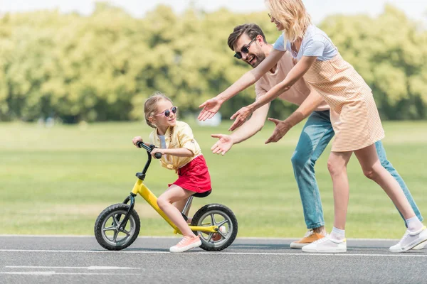 Padres felices enseñando a su hija a montar en bicicleta en el parque - foto de stock