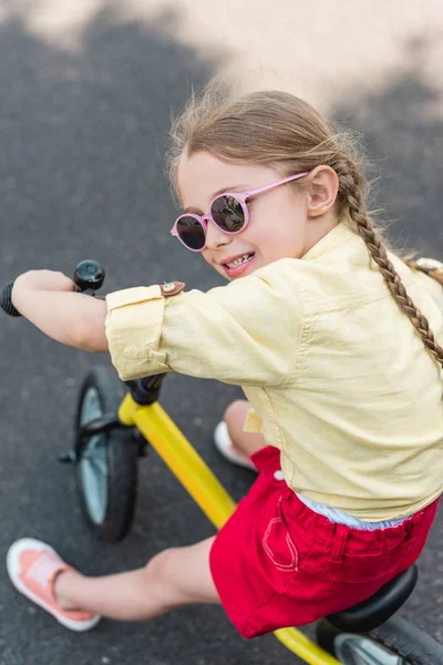 Adorable smiling child in sunglasses riding bicycle — Stock Photo