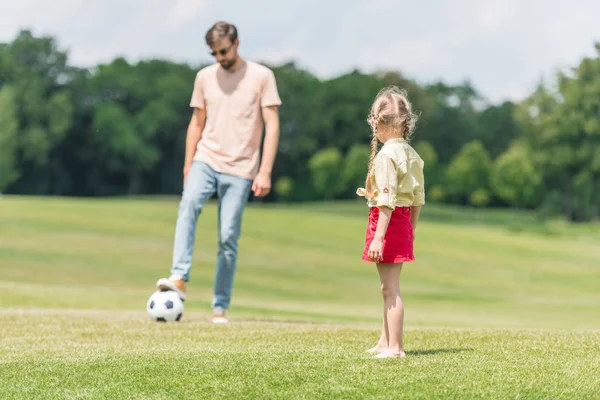 Padre y linda hija pequeña jugando con pelota de fútbol en el césped - foto de stock