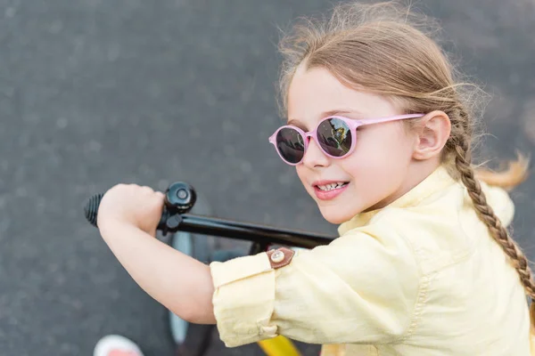 Vue rapprochée de mignon enfant souriant dans des lunettes de soleil vélo d'équitation — Photo de stock
