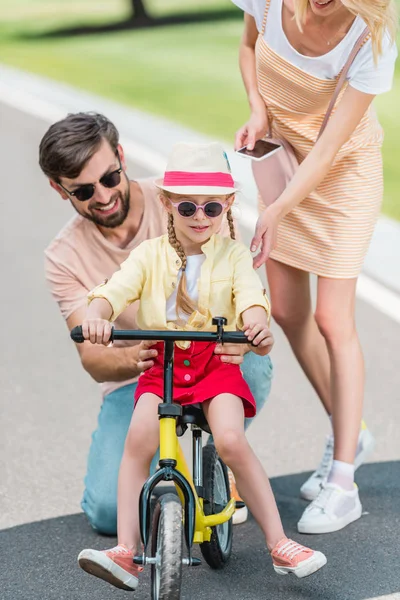 Parents heureux enseignant la petite fille à vélo dans le parc — Photo de stock