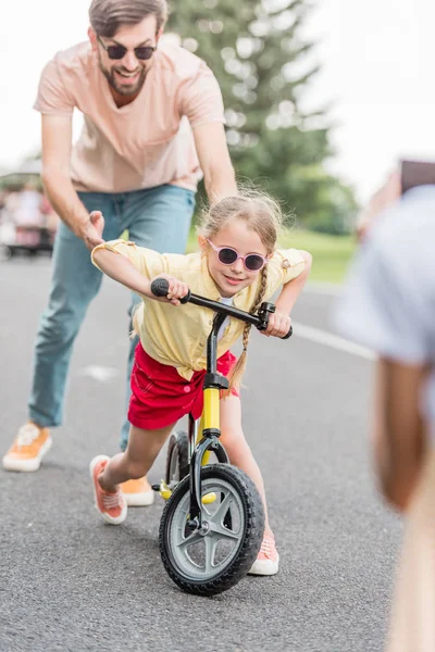 Heureux père aider petite fille à vélo dans le parc — Photo de stock