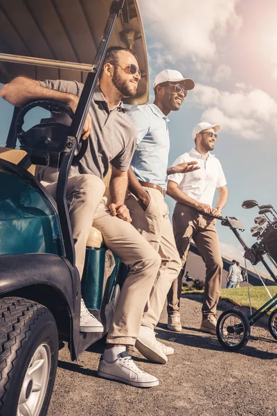 Grupo de amigos multiétnicos de pé perto do carrinho de golfe e olhando para longe — Fotografia de Stock
