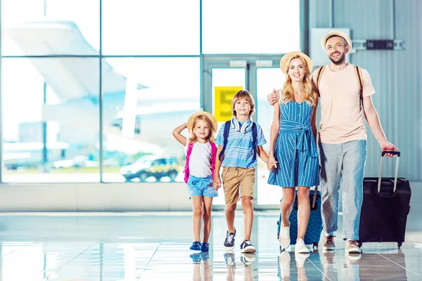 Vista frontal de la familia sonriente caminando sobre el embarque juntos en el aeropuerto, yendo de vacaciones - foto de stock