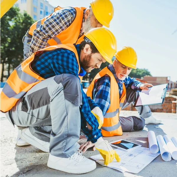 Handsome construction workers sitting on concrete at construction site, discussing building plans — Stock Photo
