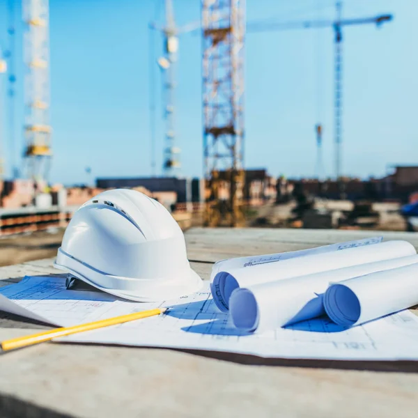 Plan rapproché de rouleaux de papier avec plans de construction et casque de sécurité sur le chantier — Photo de stock