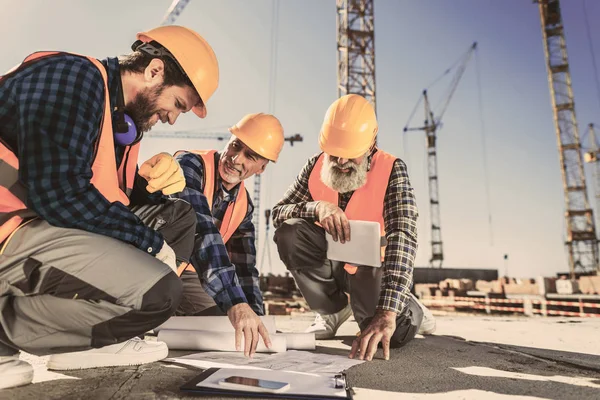 Travailleurs de la construction assis sur le béton sur le chantier et regardant les plans de construction — Photo de stock