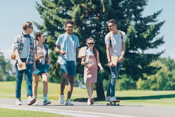 Grupo multiétnico de adolescentes hablando y caminando juntos en el parque - foto de stock
