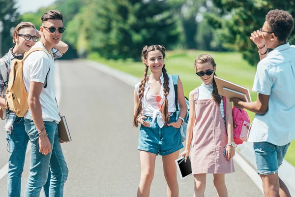 Grupo multiétnico de adolescentes com livros, mochilas e tablet digital passar tempo juntos no parque — Fotografia de Stock