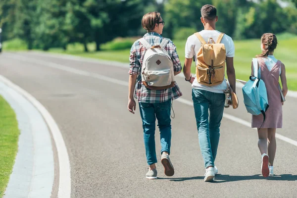 Back view of teenage students with backpacks walking together in park — Stock Photo