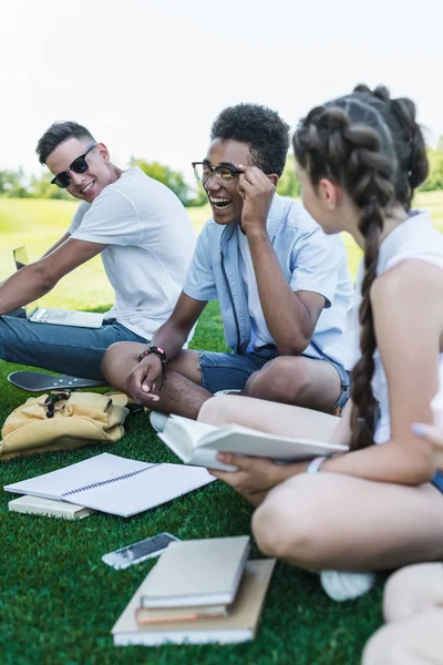 Felizes estudantes adolescentes multiétnicos sorrindo enquanto estudavam juntos no parque — Fotografia de Stock