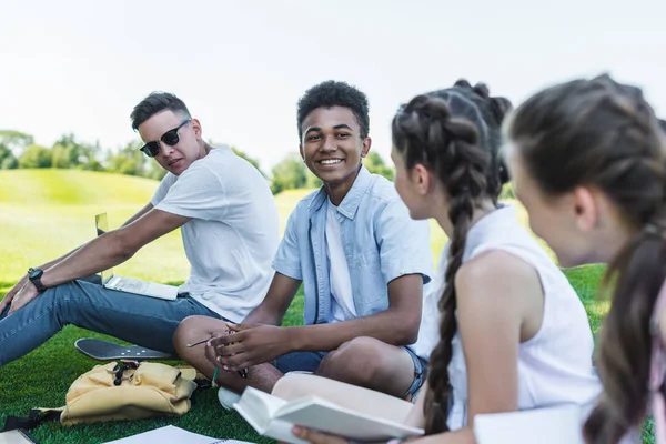 Groupe multiethnique d'étudiants adolescents se souriant tout en étudiant ensemble dans le parc — Photo de stock