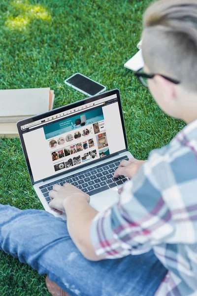 Plan recadré de l'adolescent en utilisant un ordinateur portable avec site amazone tout en étant assis dans le parc — Photo de stock