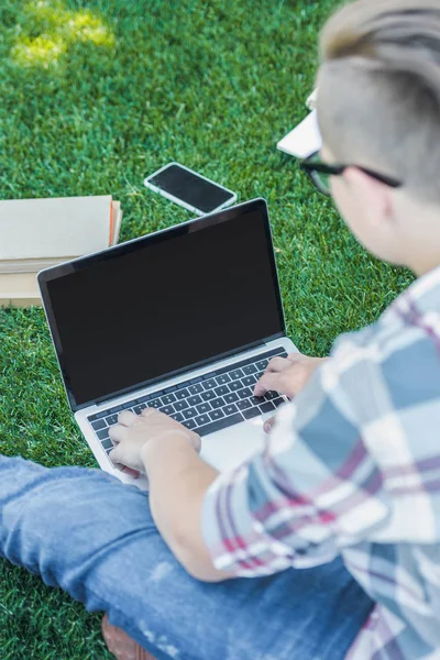 Plan recadré de l'adolescent en utilisant un ordinateur portable avec écran vierge tout en étudiant dans le parc — Photo de stock