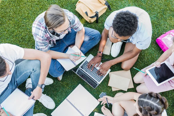 Overhead view of multiethnic teenage students studying with books and digital devices in park — Stock Photo